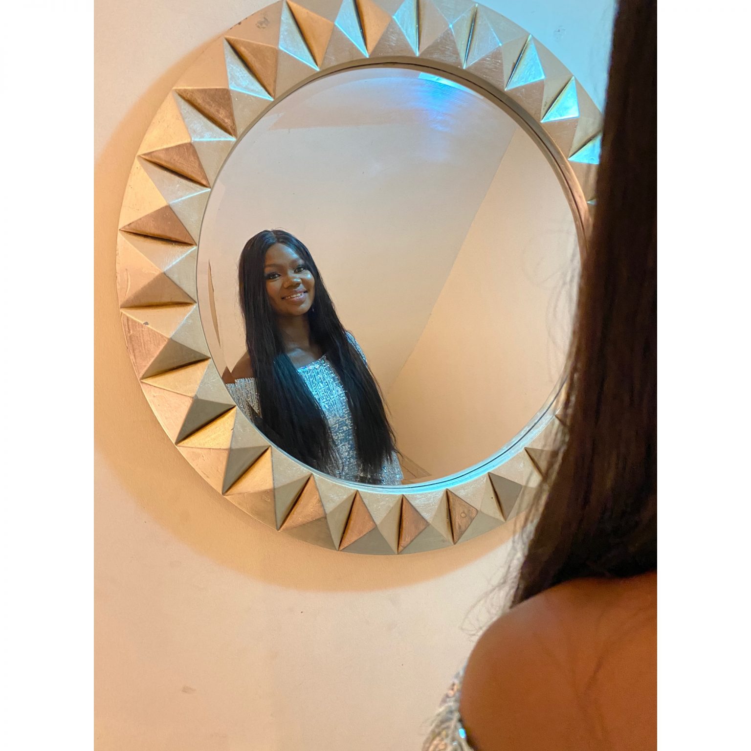 Dami in a mirror with a textured golden frame, smiling softly.